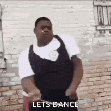 a man is dancing in front of a brick wall with the words `` let 's dance '' .
