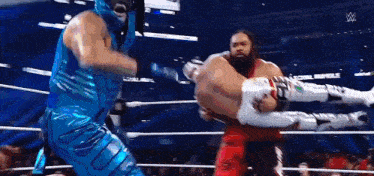 two men are wrestling in a wrestling ring and one of them is wearing a blue outfit .