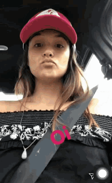 a woman wearing a red hat is sitting in a car with a pink circle around her neck that says o