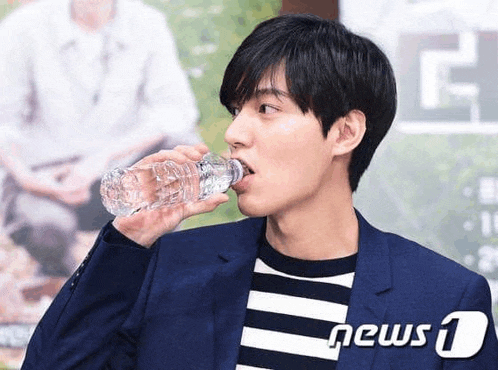 a young man in a suit is drinking water from a plastic bottle .