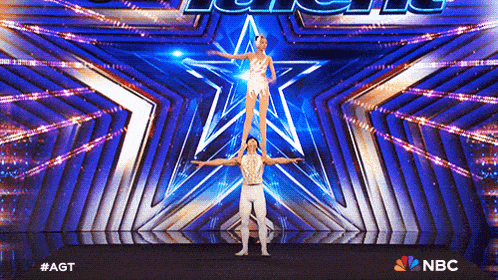 a man and a woman are standing on each other 's shoulders on a stage with a nbc logo behind them