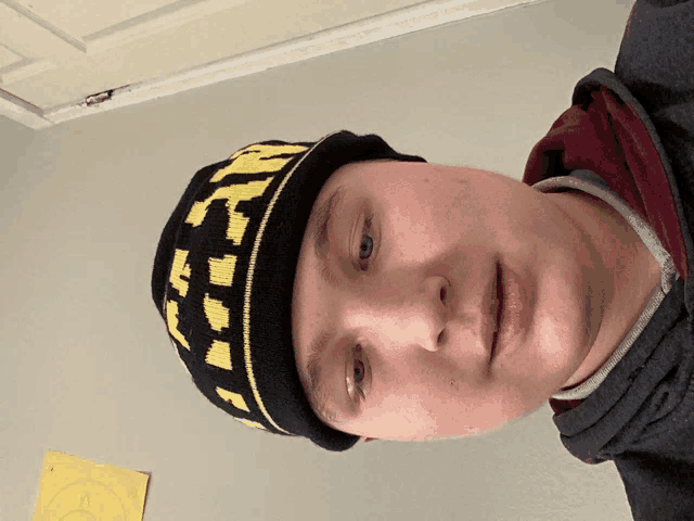 a young man wearing a black and yellow beanie with the letter t on it