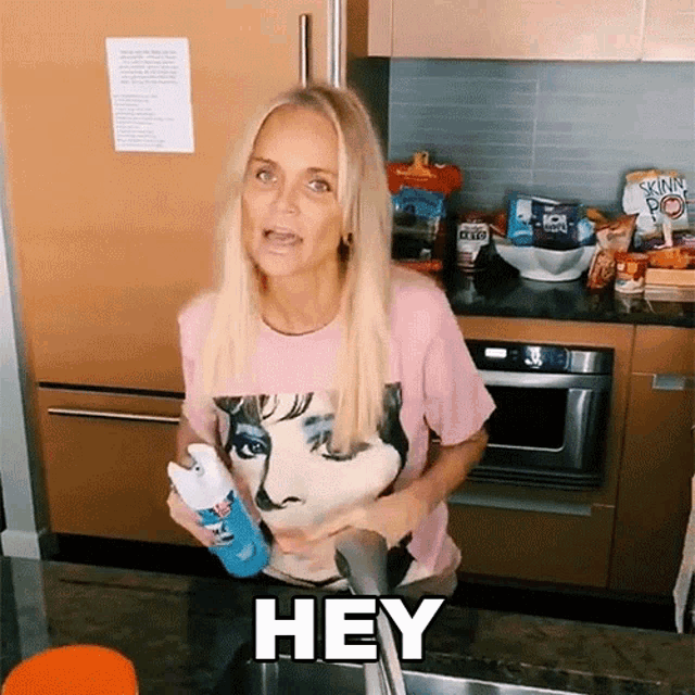 a woman in a pink shirt is holding a spray bottle and saying " hey "