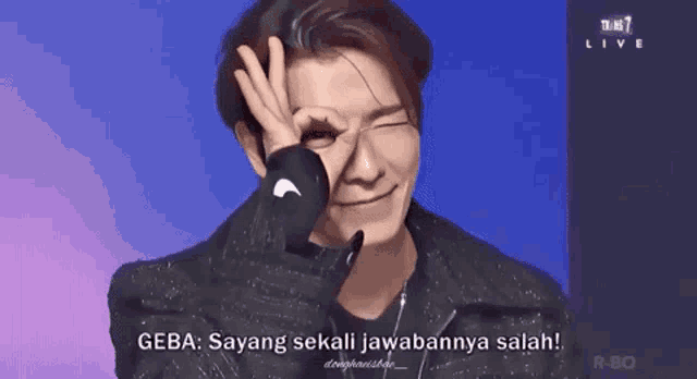 a man is making a peace sign with his hand over his eye while talking to someone .