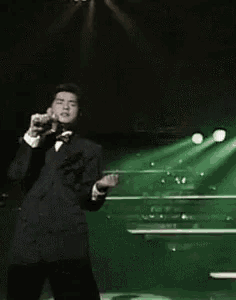a man in a tuxedo and bow tie is singing into a microphone