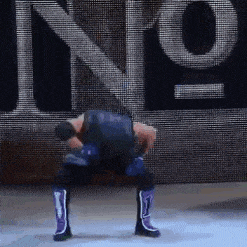 a wrestler is squatting down in front of a large screen with the word king on it .