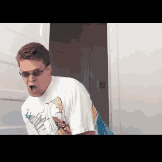 a man wearing sunglasses and a cartoon shirt is standing in a doorway with his mouth open .