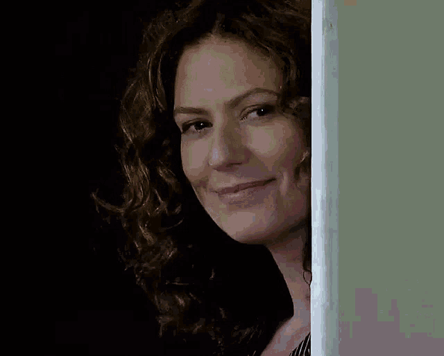 a woman with curly hair is smiling while peeking out of a doorway