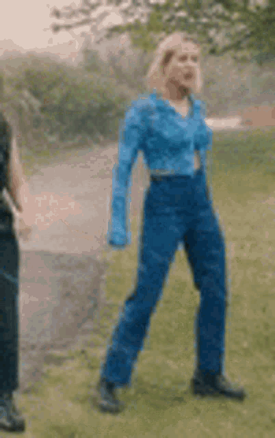 a woman in a blue jacket and blue pants is standing on a grassy field .