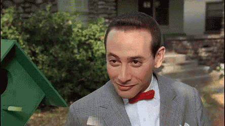 a man in a suit and red bow tie is standing in front of a green birdhouse .
