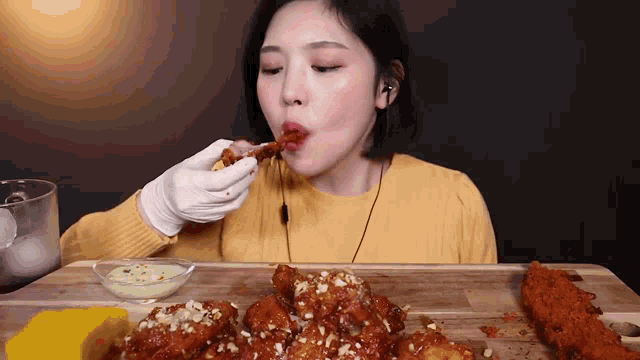 a woman in a yellow sweater is eating fried chicken on a wooden table .
