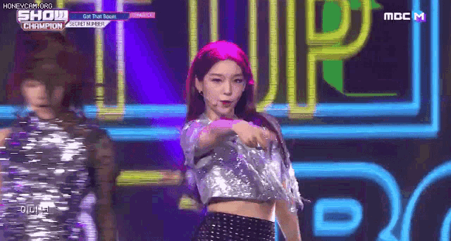 a girl with pink hair is dancing on stage in front of a neon sign that says mbc m