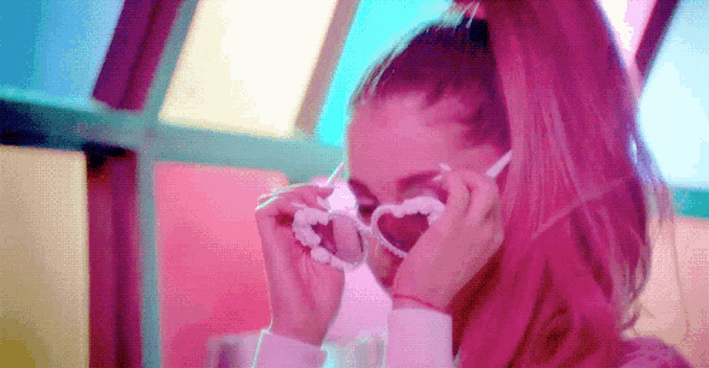 a woman with pink hair is wearing sunglasses in the shape of a heart .