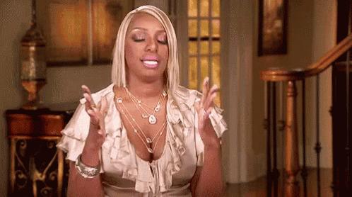 a woman in a ruffled top is sitting in a living room with her hands in the air .