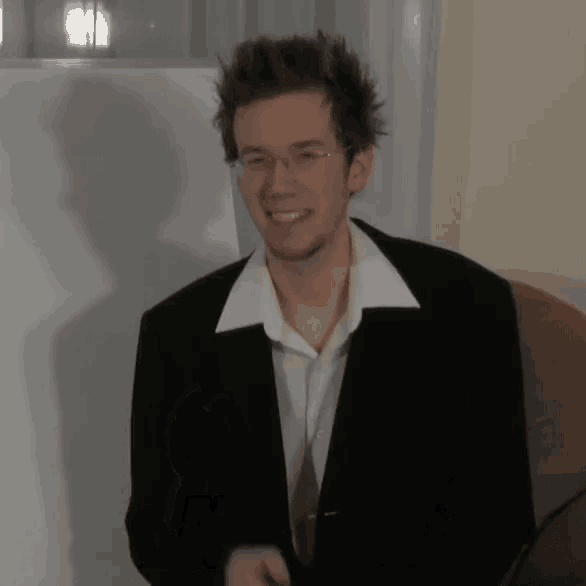 a man wearing glasses and a black jacket smiles at the camera