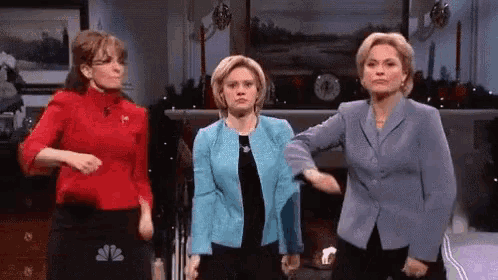 three women are standing next to each other in a room and one of them is wearing a nbc shirt