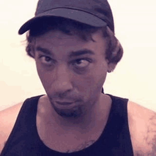 a man wearing a hat and a tank top is making a face .