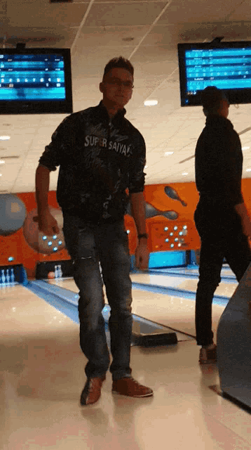 a man in a super saiyan shirt holds a bowling ball in a bowling alley