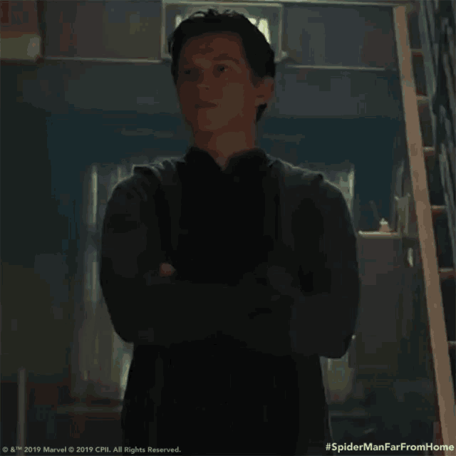 a man is standing in a hallway with his arms crossed and a green exit sign in the background .