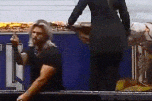 a man is kneeling down in front of a blue wall while a woman is standing behind him .