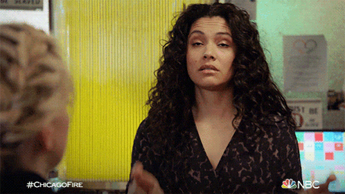 a woman with curly hair is standing in front of a yellow wall with a sign that says " do not enter "