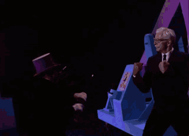 a man in a suit and tie is standing next to a man in a purple top hat .