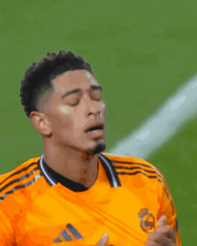 a soccer player wearing an orange adidas jersey looks down