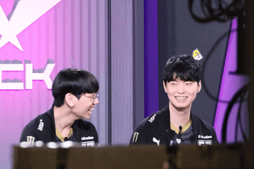 two young men are smiling in front of a sign that says ' ck ' on it