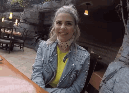 a woman wearing a studded denim jacket sits at a restaurant table