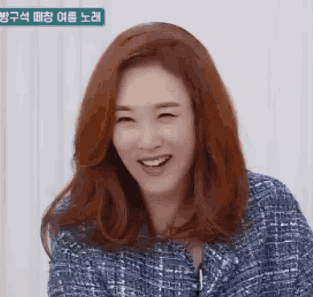 a woman with red hair is smiling with her eyes closed and wearing a blue sweater .