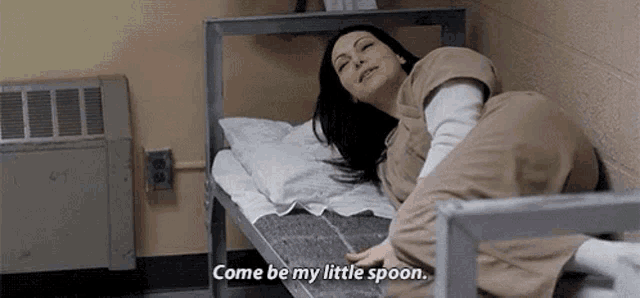 a woman is laying on a bed in a prison cell and says `` come be my little spoon '' .