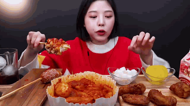 a woman in a red sweater is eating a variety of food on a table .
