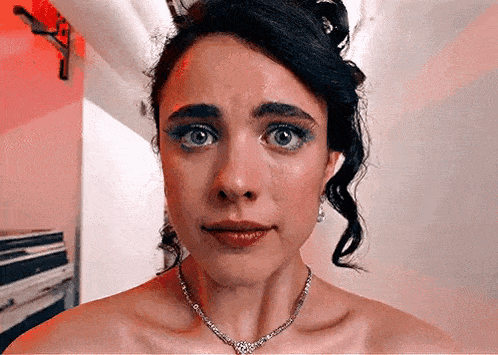 a woman in a white dress and necklace is making a funny face .