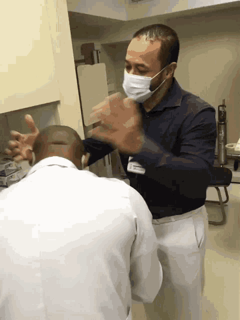 a man wearing a mask talks to another man in a lab coat