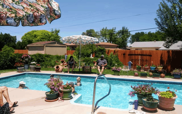 a man sits on the edge of a swimming pool with a floral umbrella