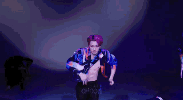 a man with purple hair is dancing on a stage in a dark room .