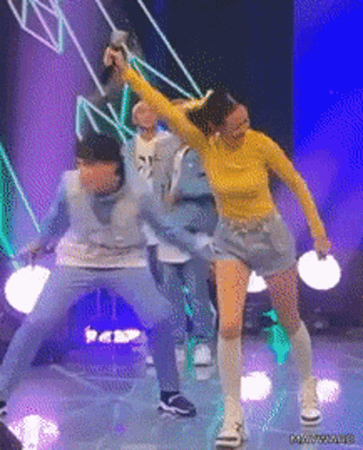 a group of people are dancing on a stage and one of them is wearing a yellow shirt and shorts