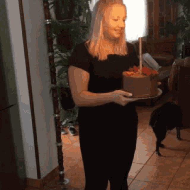 a woman in a black dress is holding a birthday cake