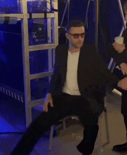 a man wearing sunglasses is sitting on a stool