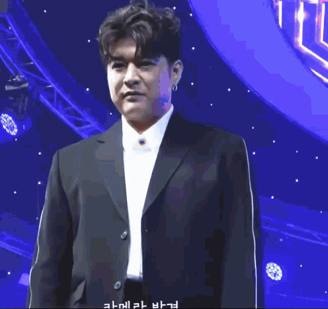 a man in a black suit and white shirt is standing in front of a blue background .