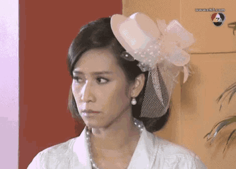 a woman wearing a white hat with a veil and pearls looks at the camera