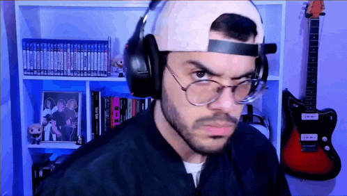 a man wearing headphones and glasses looks angry in front of a guitar