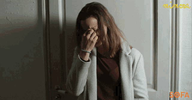 a woman covering her face in front of a door that has the word sofa on it