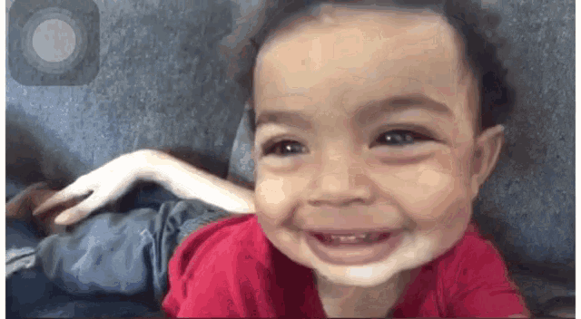 a baby in a red shirt is smiling while sitting on a plane