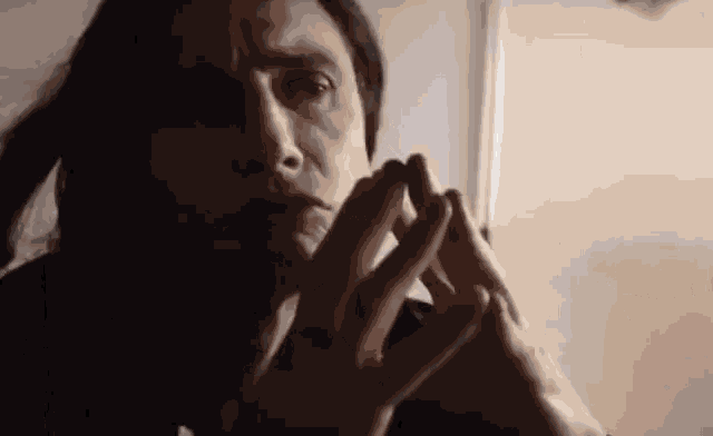 a close up of a person 's face with their hands folded in front of them .