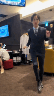 a man in a suit is dancing in a room with a tv on the wall .