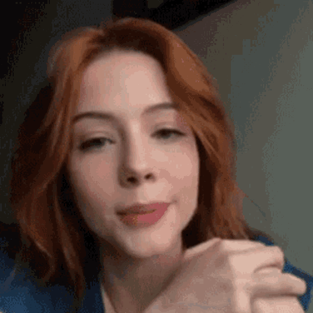 a close up of a woman 's face with red hair and a blue shirt .