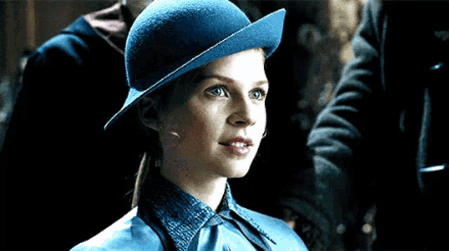 a woman wearing a blue hat and a blue shirt is standing in a dark room .