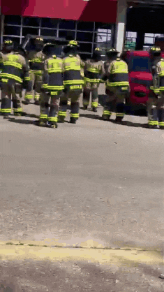 a group of firefighters are standing in a line on the sidewalk in front of a fire station .