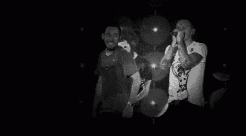 a black and white photo of a man singing into a microphone on a stage in a dark room .